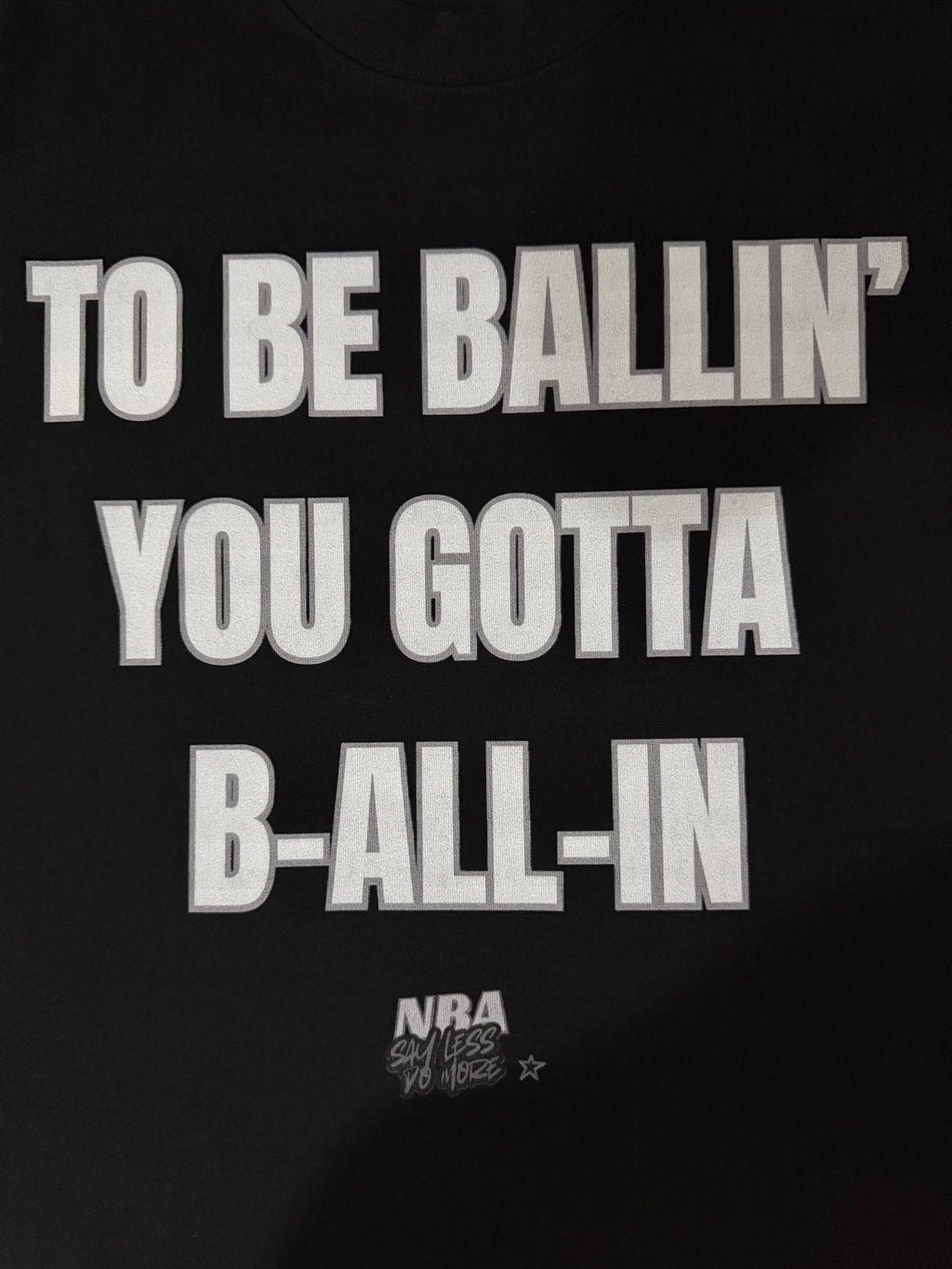 Black “ALL-IN” T-shirt by NBASayLessDoMore, front view showing casual fit and bold printed design on soft cotton fabric.